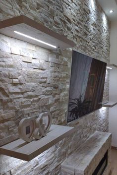 a tv mounted on a stone wall next to a shelf with candles and other items