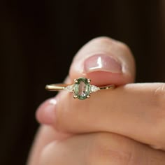 a close up of a person's hand holding a ring with an oval green stone