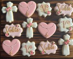 decorated cookies in the shape of hearts and cross with name written on them, arranged on a wooden surface