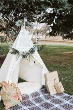 a teepee tent is set up on the grass with presents under it and trees in the background