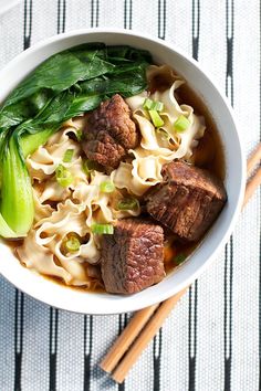 a bowl filled with noodles, meat and vegetables next to chopsticks on a table