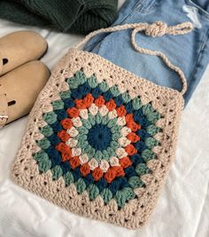 a crocheted bag sitting on top of a bed next to jeans and shoes