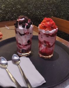 two desserts are sitting on a plate with spoons next to eachother