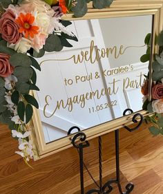 a welcome sign with flowers and greenery is displayed in front of a mirror that reads, welcome to paul & karolee's engagement party