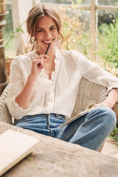 a woman sitting on a chair holding a pen in her right hand and smiling at the camera