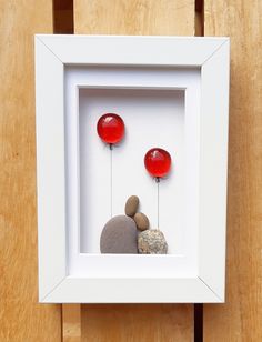 a white frame with some rocks and two red balloons