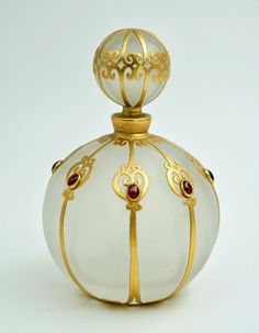 a white glass bottle with gold trimmings and a red stone in the top