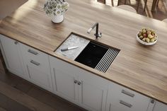 a kitchen sink sitting on top of a wooden counter next to a bowl of fruit