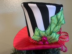 "This is a Christmas tree topper top hat and or centerpiece and is all finished and READY TO BE SHIPPED. The top hat tree topper/centerpiece is made as follows: *The taper/body is made with black and white striped fabric. *The band is made with hot pink polka-dot ribbon. * Decorated with holly leaf's and hot pink berries and a loops of ribbon at the back. *The brim is made with 1.5\" wide hot pink ribbon. The top hat is uniquely made with a cavity opening on the top and bottom that sits firmly o Whimsical Tree Topper, Top Hat Christmas Tree Topper, White Tree Topper, Top Hat Christmas Tree, Hat Christmas Tree Topper, Top Hat Centerpieces, Top Hat Tree Topper, Whimsical Tree, Centerpiece Christmas