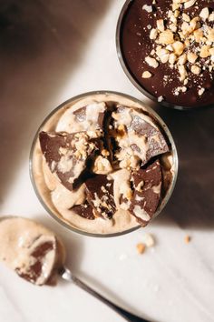 two desserts with chocolate and peanut butter in them on a white tablecloth next to a spoon