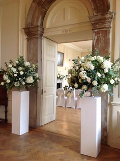 two tall vases with white flowers are on display in front of an open door