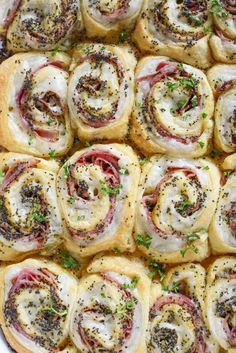 a tray filled with rolls covered in meat and cheese on top of each other, topped with parsley