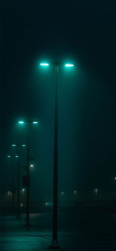 an empty parking lot at night with street lights on the sides and fog in the air