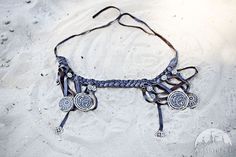 a necklace is laying on the sand with two medallions and beads hanging from it