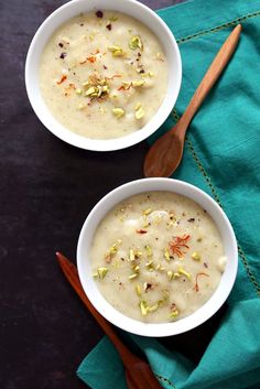 two white bowls filled with soup on top of a green cloth next to wooden spoons