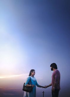 a man and woman standing next to each other holding hands with the sky in the background