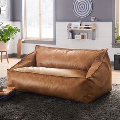 a large brown leather couch sitting on top of a carpeted floor next to a window