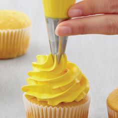 a cupcake being frosted with yellow icing by a person using a piping tool