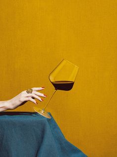 a woman's hand reaching for a glass of wine in front of a yellow wall