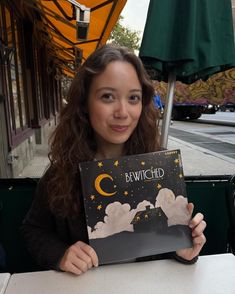 a woman sitting at a table holding up a card that reads bewitchd