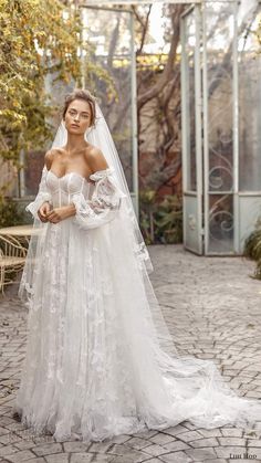 a woman in a white wedding dress standing on a cobblestone walkway wearing a long veil