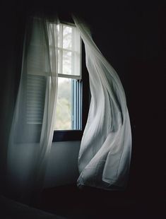 an open window in a dark room with sheer curtains