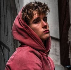 a young man in a red hoodie is leaning against a wall and looking off into the distance