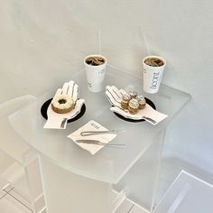 two plates with donuts on them sitting on a clear table next to coffee cups and utensils