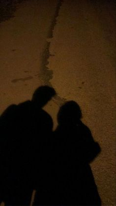 two people standing next to each other in the street at night with their shadows on the ground