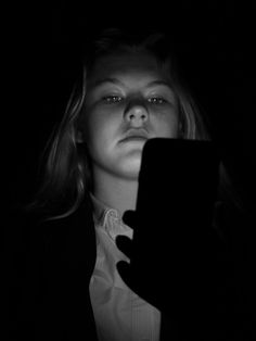 a woman holding a tablet in the dark with her hands on her face and looking at it