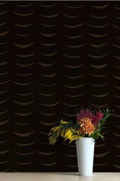 a white vase filled with colorful flowers on top of a wooden table next to a black wall