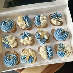 twelve cupcakes with blue and white frosting in a box on a table