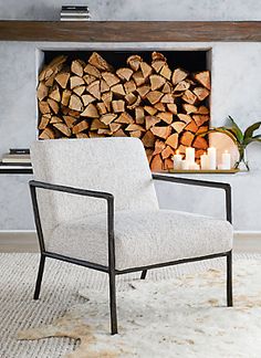 a chair sitting in front of a fire place filled with logs and lit candles next to a fireplace