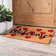 a welcome mat with hearts on it sitting next to a potted plant in front of a door