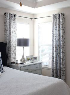 a white bed sitting in a bedroom next to a window with drapes on it