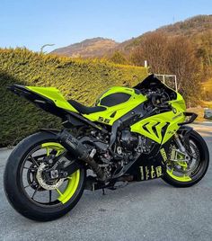 a yellow and black motorcycle parked in front of a hedged area with mountains behind it