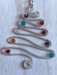 a christmas tree made out of silver wire and colored glass beads on a white wooden surface