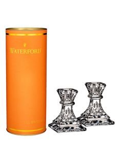 two crystal candlesticks are next to an orange canister with the word waterfoord on it