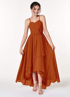 a woman is wearing an orange dress with straps on the waist and side, she has her hands in her pockets