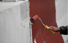 a person using a paint roller to paint a red wall with white paint on it