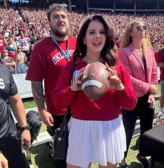 a woman holding a football while standing next to a man in a red shirt and white skirt