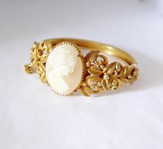 "This ornate vintage Florenza 24K gold plated bracelet features a hand carved cameo flanked by a botanical, renaissance style design. The back is delicately etched with a continual floral design. Daniel Kasoff founded Dan Kasoff Corporation as a costume jewelry company in 1937. In 1950 his son joined the company and the name changed to Florenza as a tribute to Daniel's wife, Florence. Daniel and Larry both designed most of the Florenza jewelry pieces. The line specialized in 24K gold plated brac Elegant Carved Oval Jewelry, Elegant Oval Carved Jewelry, Antique Gold Bracelet For Gift, Ornate Cameo Jewelry For Anniversary, Elegant Antique Gold Bangle Bracelet, Formal Intaglio Bangle Jewelry, Antique Carved Yellow Gold Jewelry, Ornate Cameo Jewelry For Formal Occasions, Elegant Antique Gold Bracelet