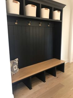 a wooden bench with four white baskets on it's back and three black shelves