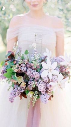 a woman holding a bouquet of flowers in her hands and wearing a dress with sheer sleeves