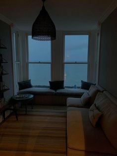 a living room filled with furniture next to a large window overlooking the ocean at night