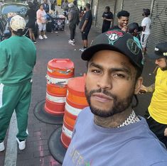 a man with tattoos on his face standing in front of traffic cones and people walking down the street