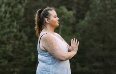 a woman standing in front of some trees with her hands together and looking up to the sky