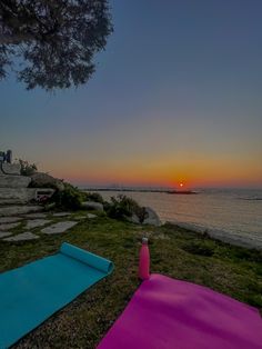 two yoga mats are sitting on the grass by the water as the sun goes down