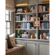 a bookshelf filled with lots of books next to a window covered in pillows