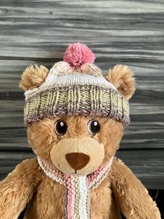 a brown teddy bear wearing a knitted hat and scarf with a pink pom - pom